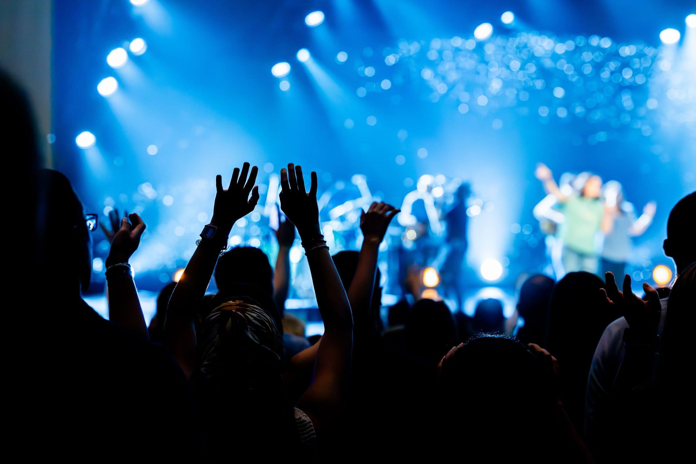 A crowd, hands up, under blue stage light