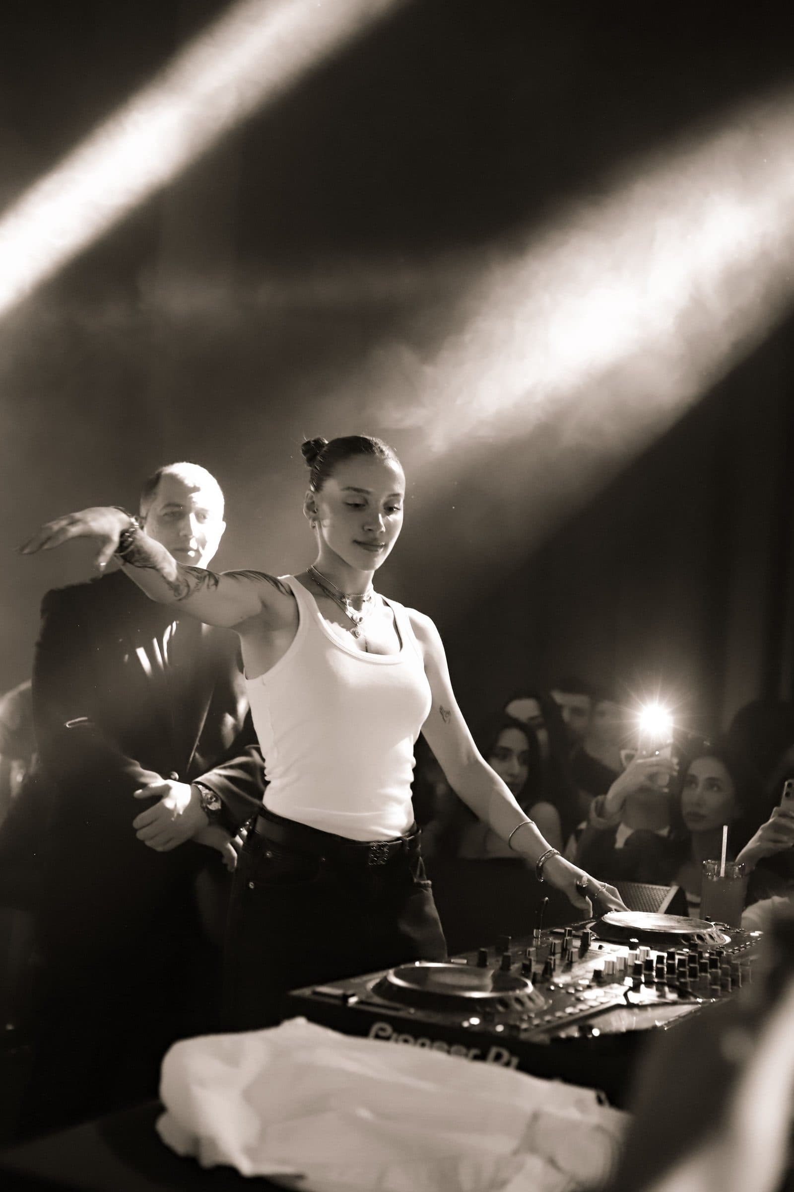 A DJ at the decks, the crowd behind them under the lights