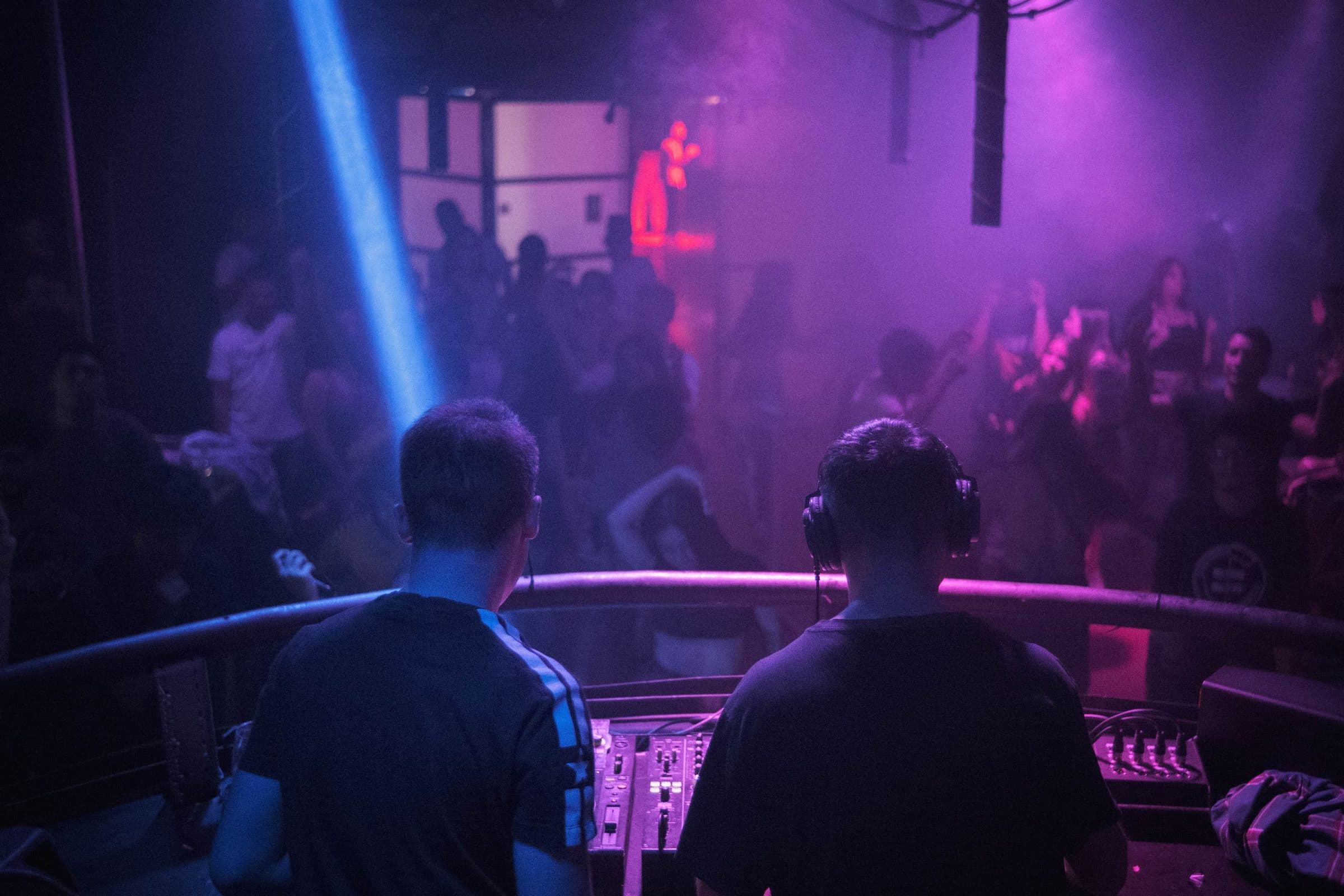 Two DJs from behind, a lit room in front of them